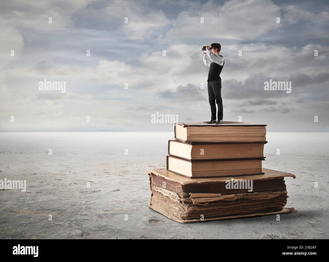 Businessman on books looking with telescope Stock Photo - Alamy