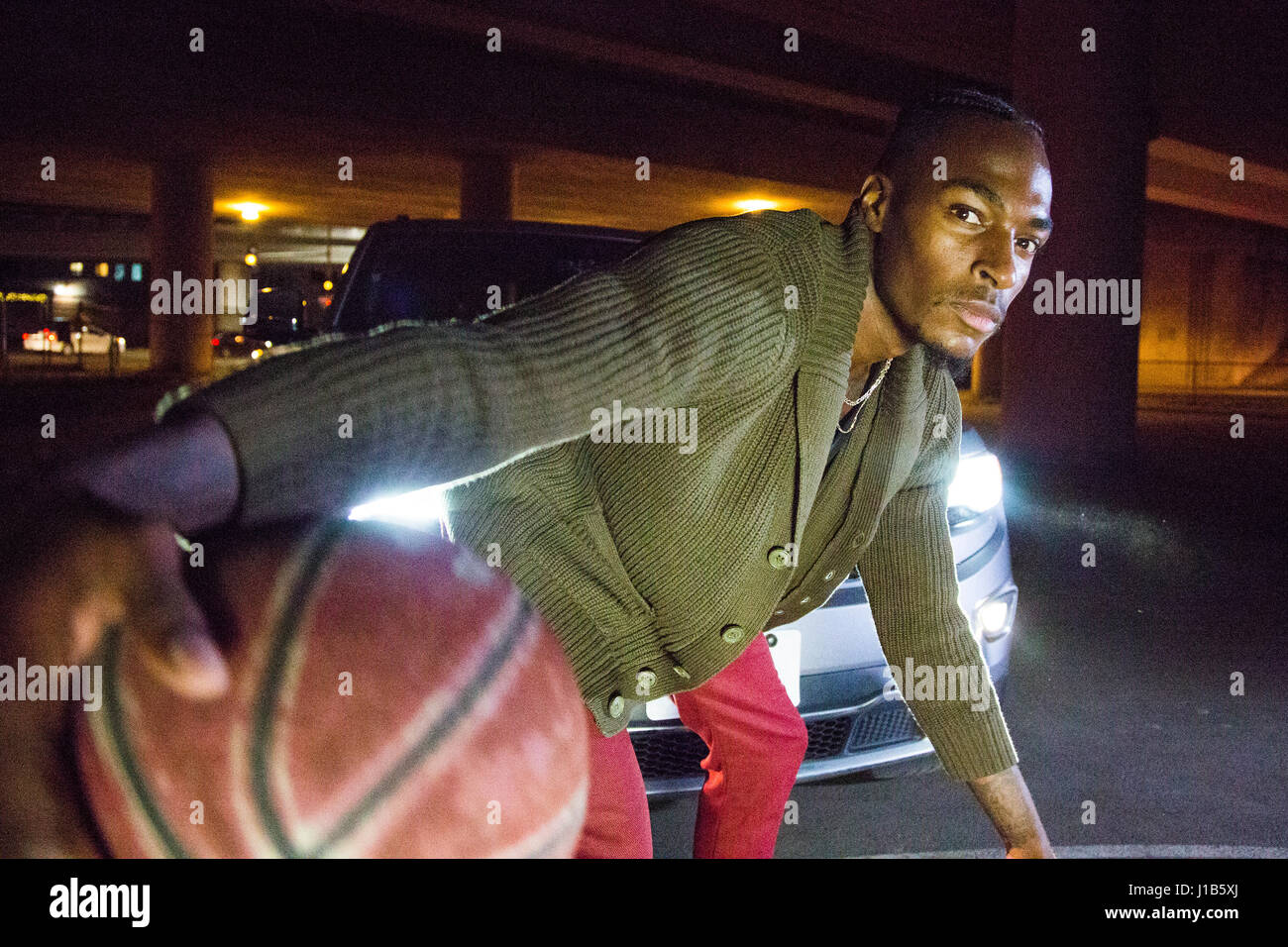 Headlights shining on Black man playing basketball Stock Photo