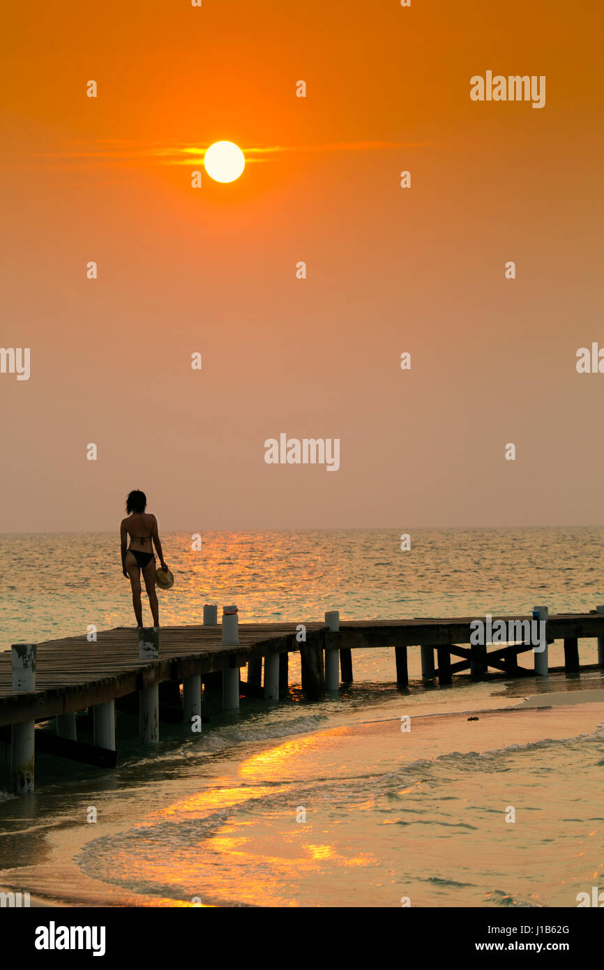 Mixed Race woman standing on ocean dock at sunset Stock Photo