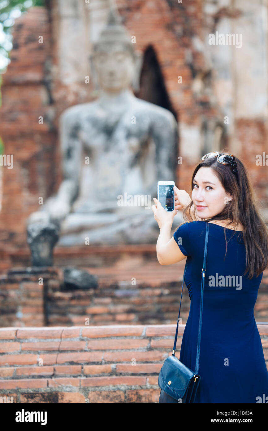 Asian woman photographing Buddha statue with cell phone Stock Photo