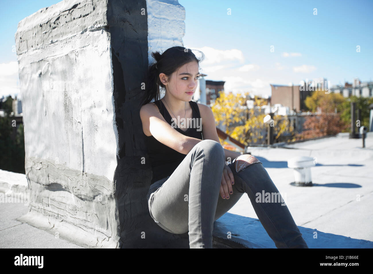 Caucasian girl sitting on rooftop Stock Photo