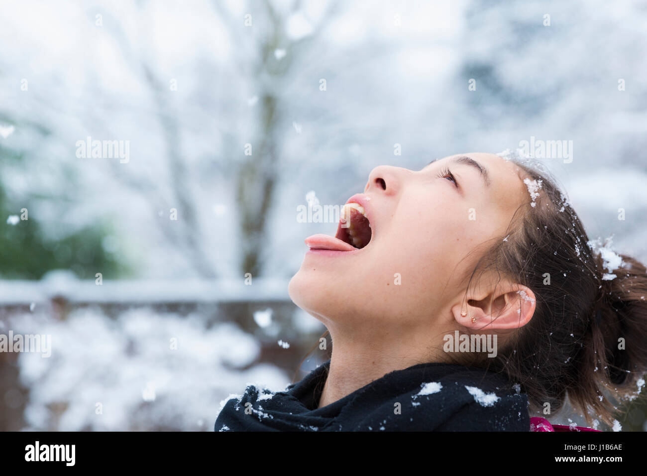 Mixed Race girl catching snowflakes on tongue Stock Photo