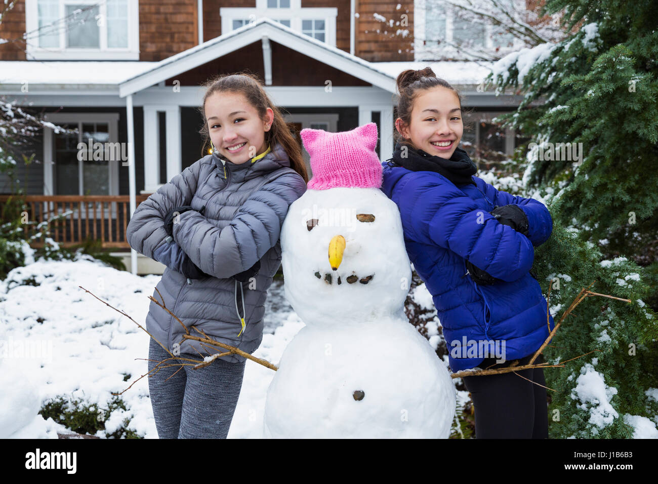 Mixed Race girls posing with snowman wearing pink hat with ears Stock Photo