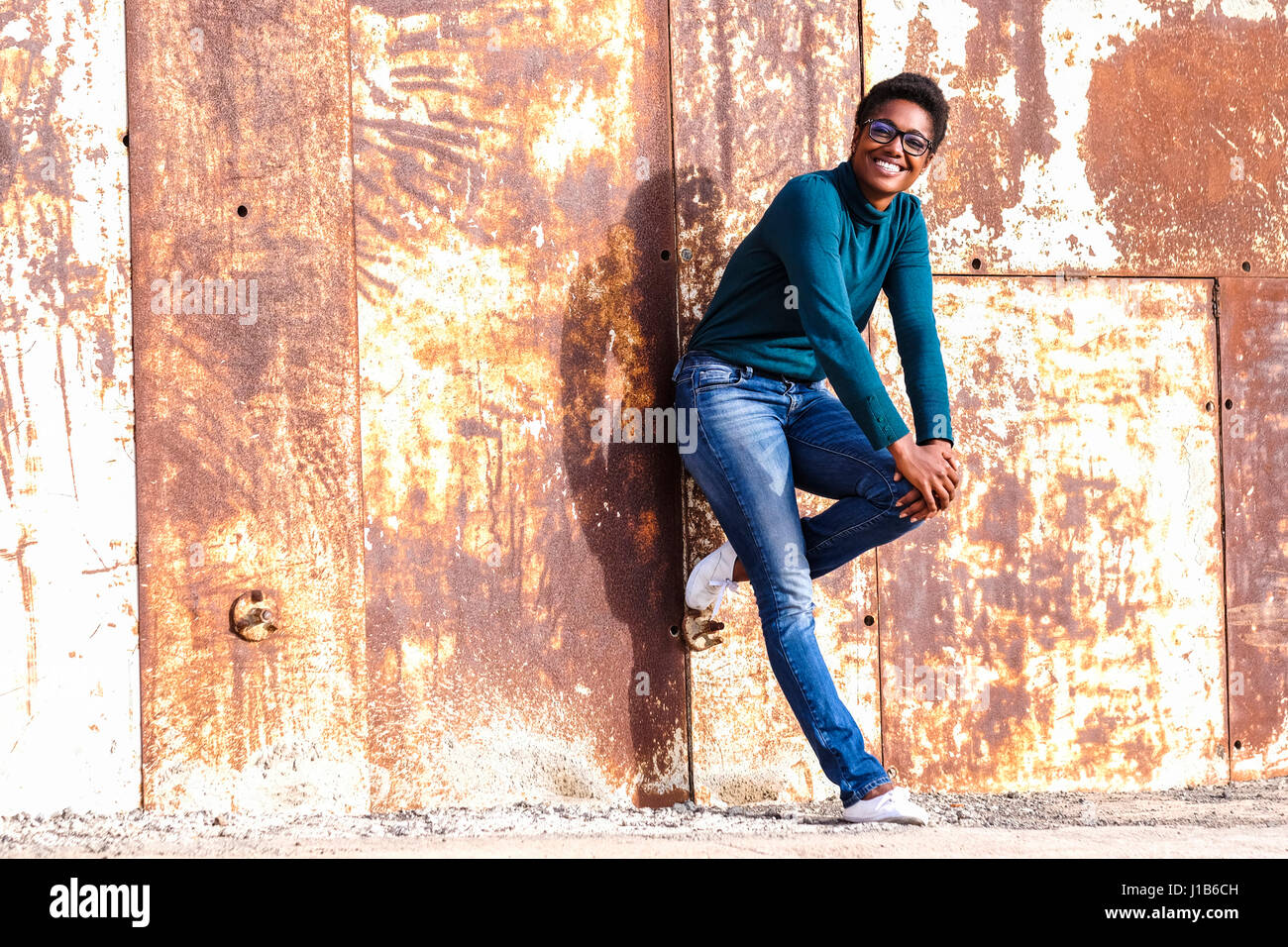 African American woman leaning on rusty metal wall Stock Photo