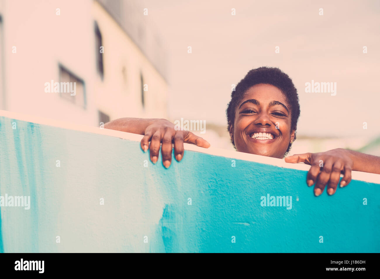 Smiling African American woman peering over blue wall Stock Photo