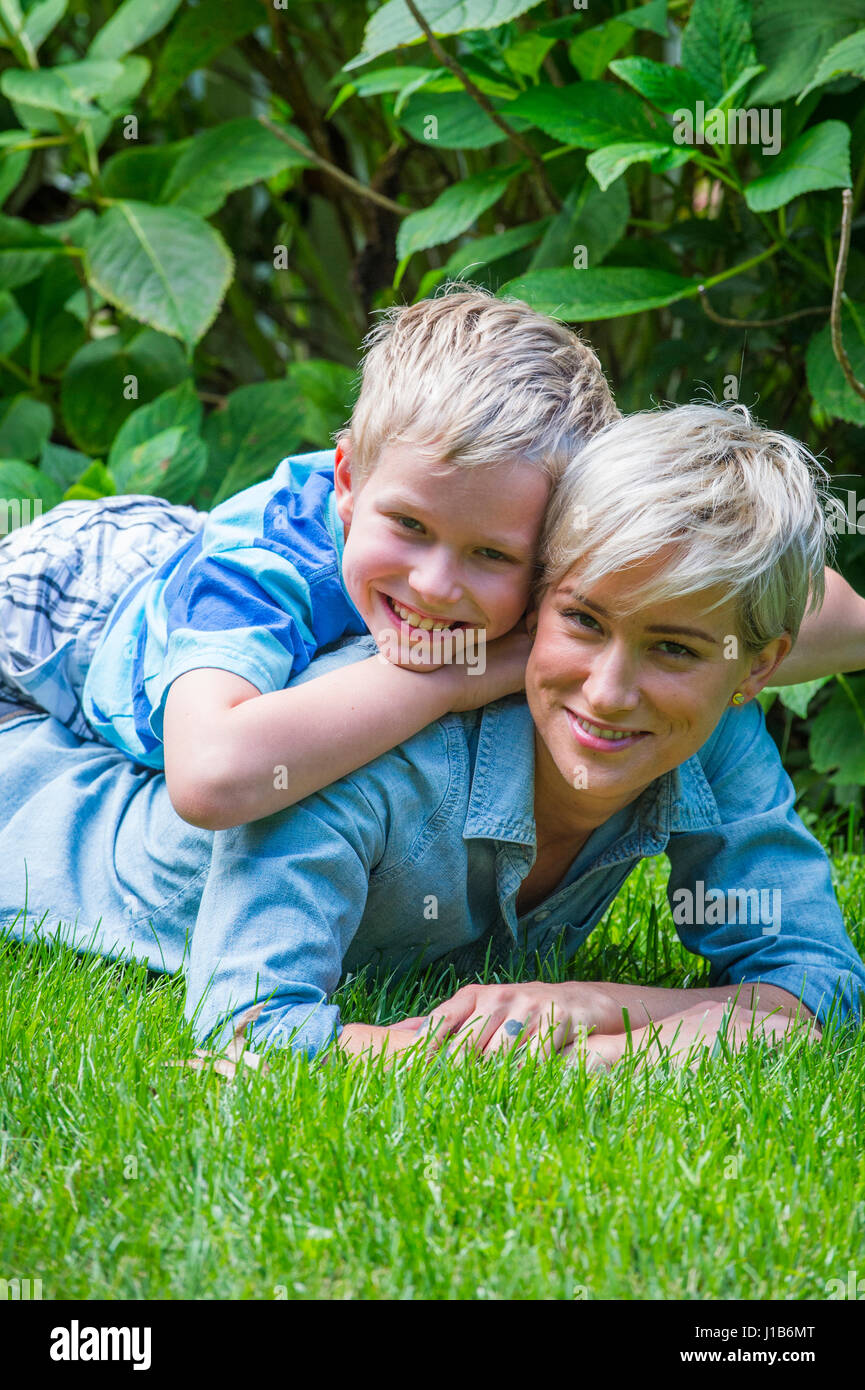 Caucasian boy laying on back of mother in grass Stock Photo