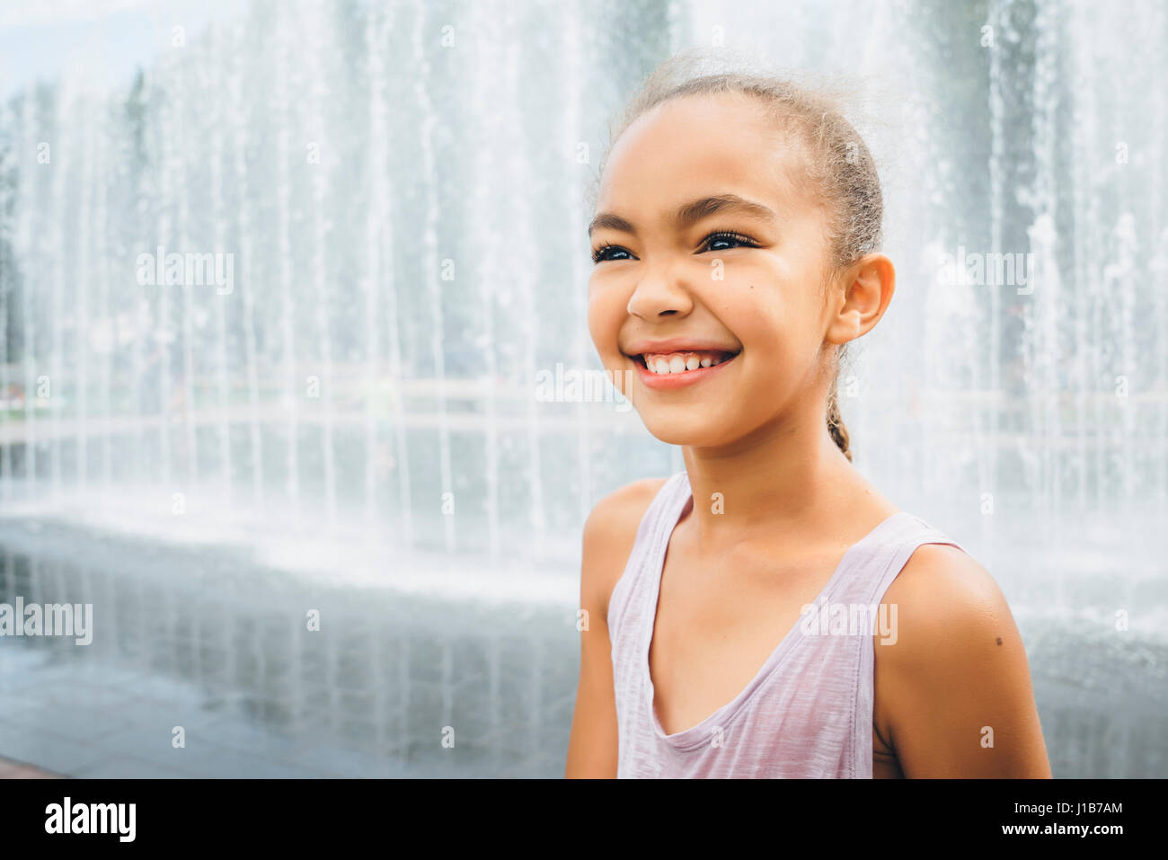 Smiling Mixed Race girl near fountain Stock Photo