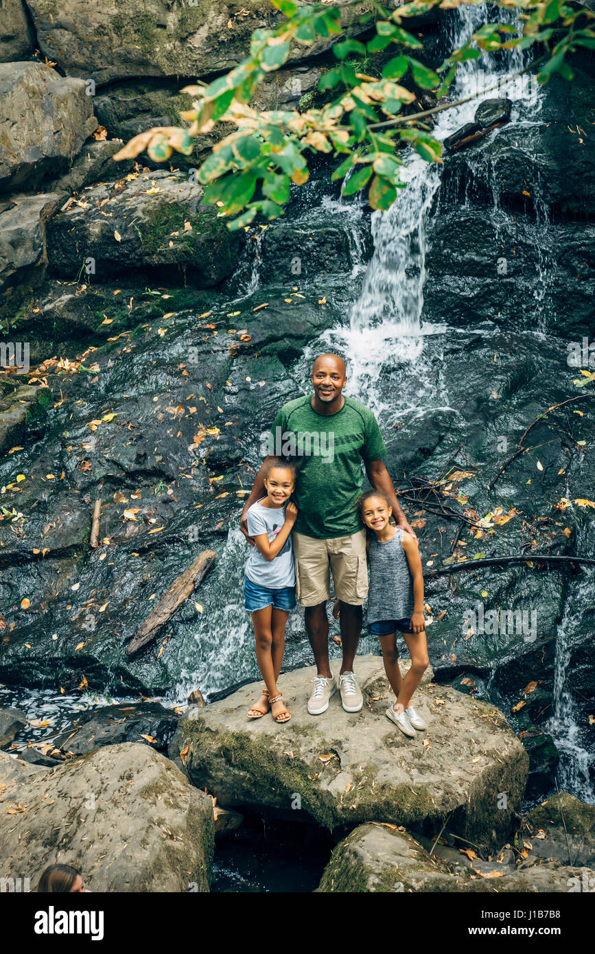 Father and daughters posing on rock near waterfall Stock Photo