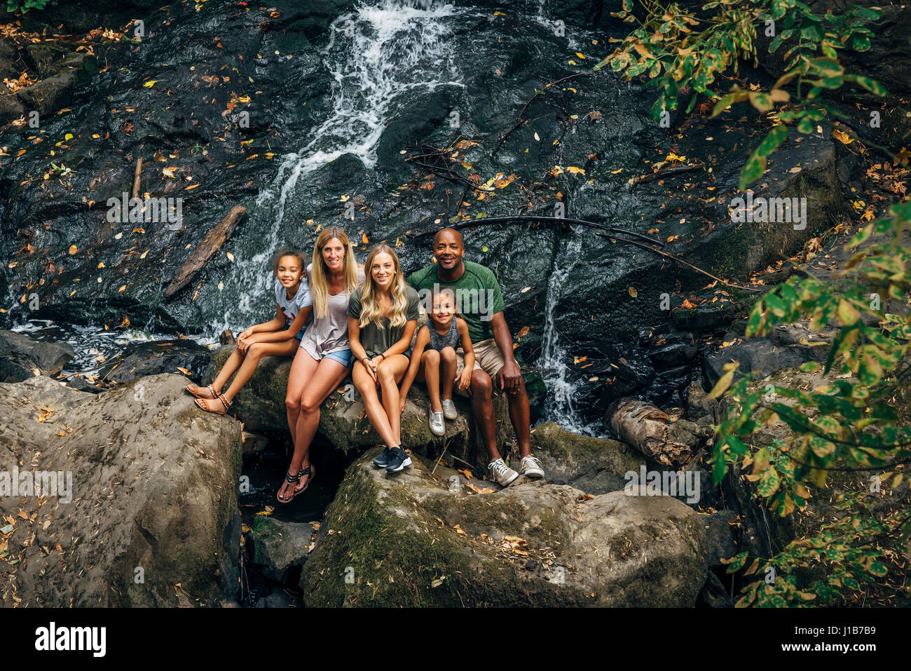 Multi-ethnic family posing on rock near waterfall Stock Photo
