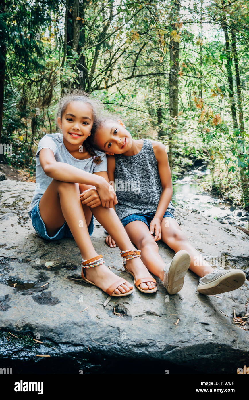 Portrait of smiling Mixed Race girls sitting on rock Stock Photo