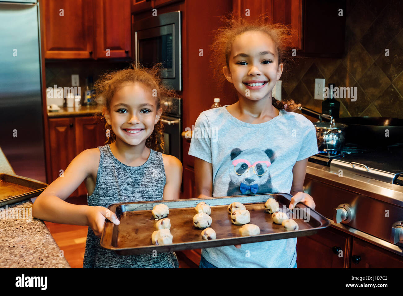 Mixed Race girls holding tray with cookie dough in domestic kitchen Stock Photo