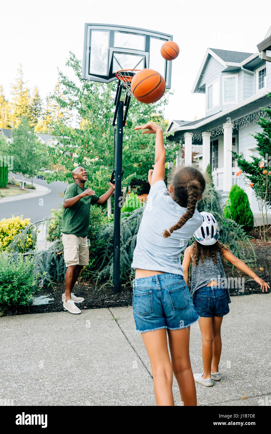 Father and daughters playing basketball in driveway Stock Photo