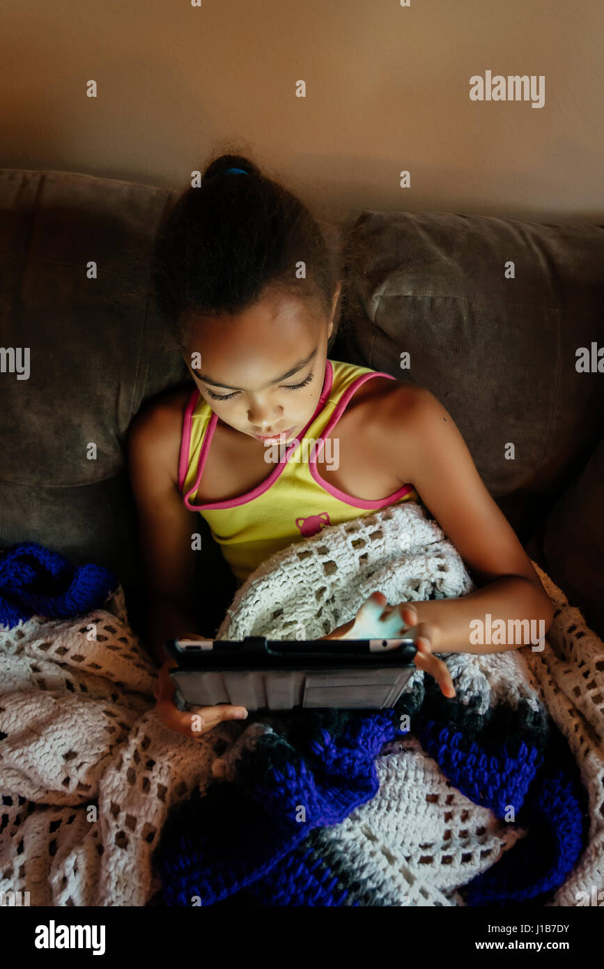 Mixed Race girl using digital tablet on sofa at night Stock Photo