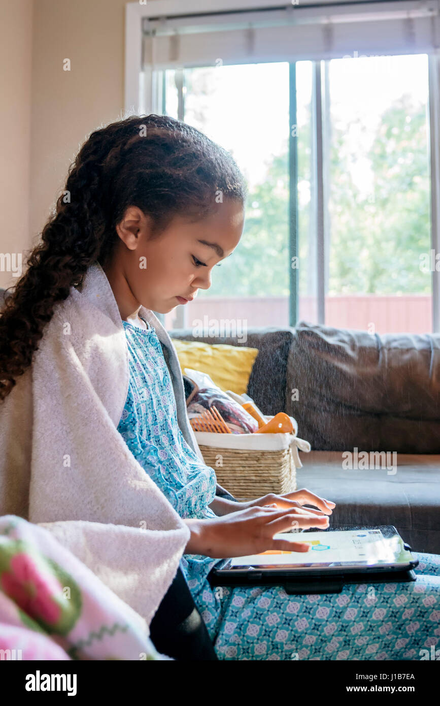 Mixed Race girl using digital tablet on sofa Stock Photo