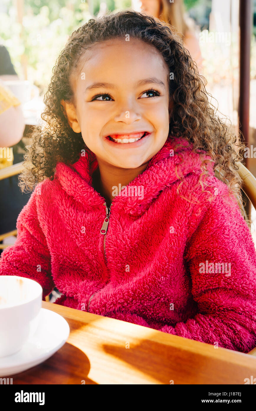 Smiling Mixed Race girl sitting at restaurant table Stock Photo