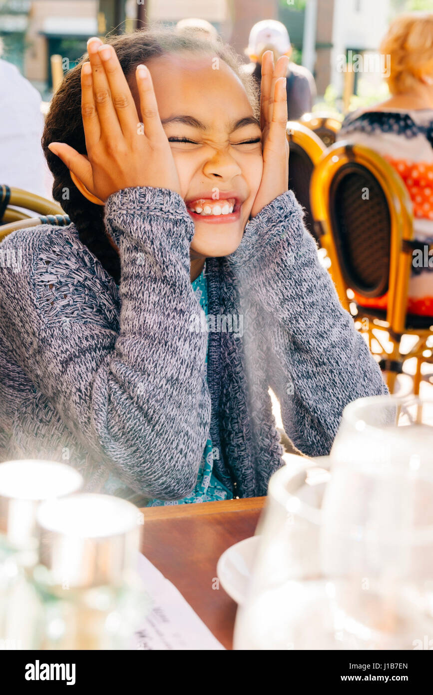 Smiling Mixed Race girl making a face at restaurant table Stock Photo
