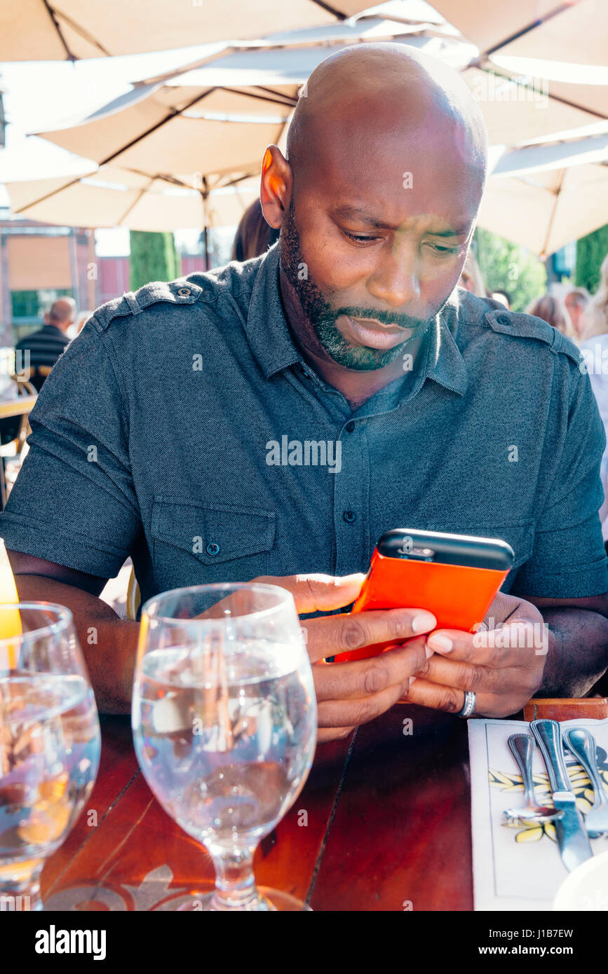 Black man sitting at restaurant table texting on cell phone Stock Photo