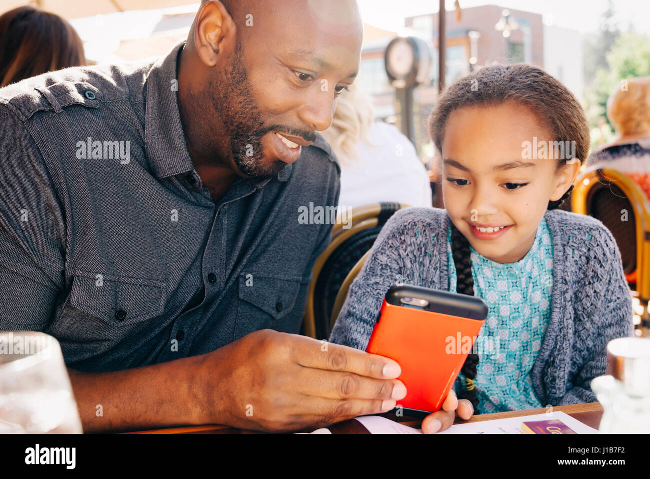 Father and daughter sitting at restaurant table texting on cell phone Stock Photo