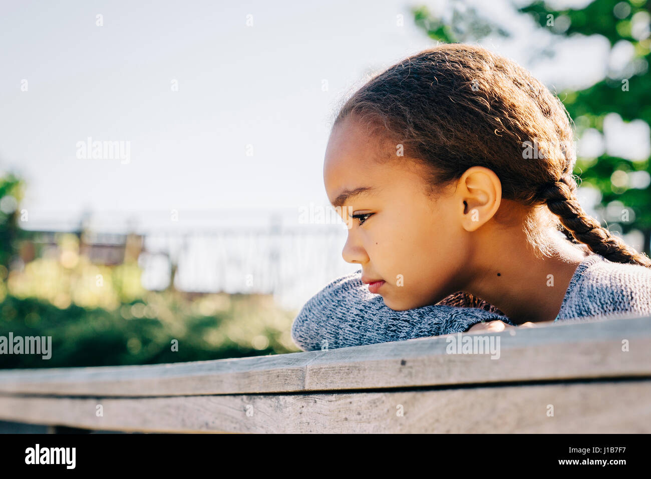 Pensive Mixed Race girl leaning on wooden railing Stock Photo