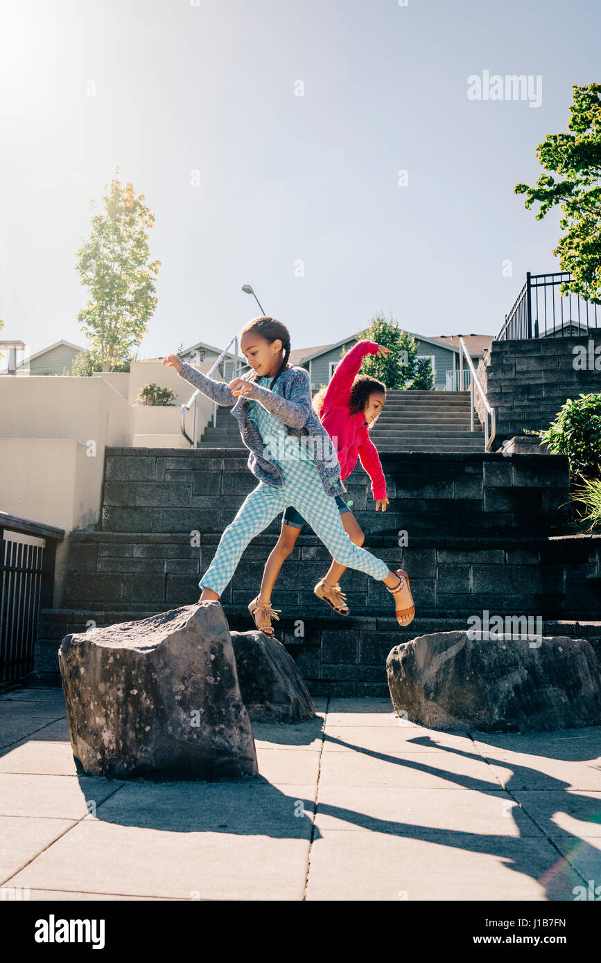 Mixed Race sisters jumping on rocks Stock Photo
