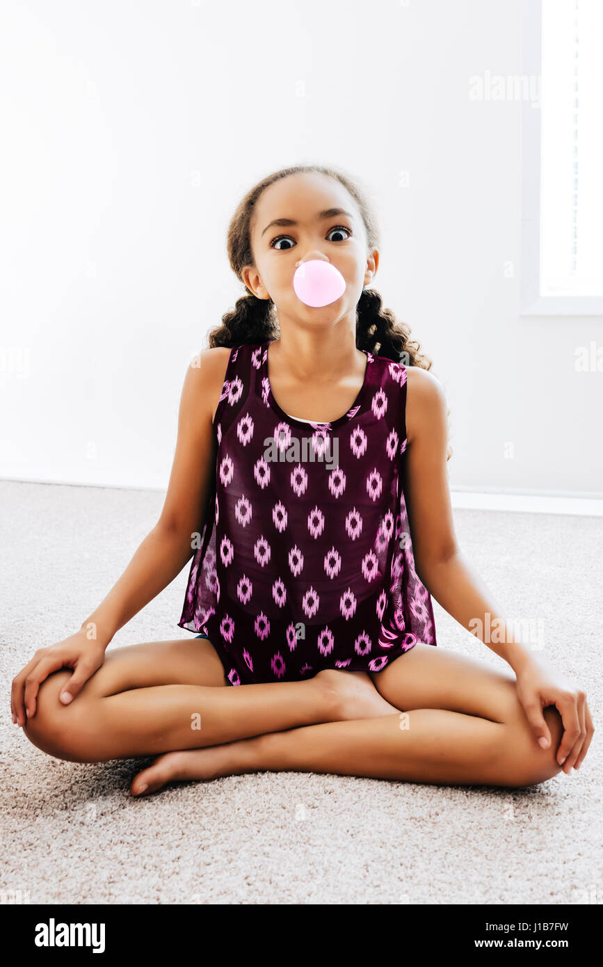 Mixed Race girl sitting on floor blowing bubble with gum Stock Photo