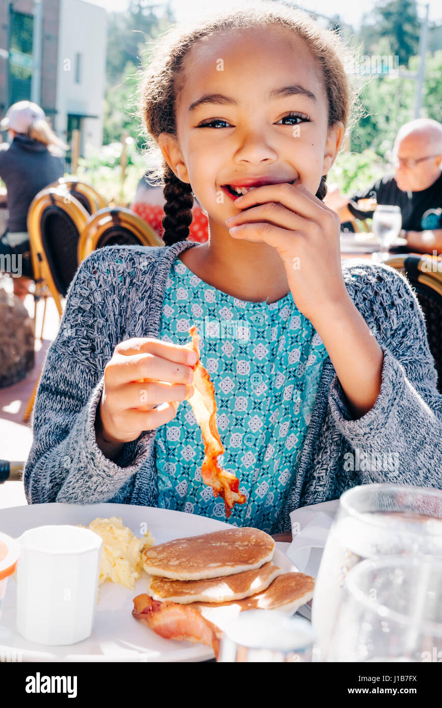 Smiling Mixed Race girl eating breakfast at restaurant Stock Photo