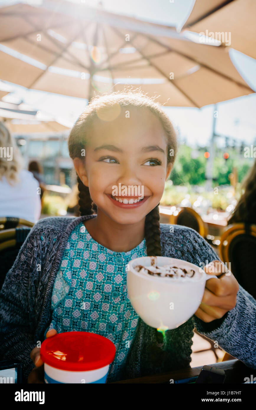 Smiling Mixed Race girl drinking from cup in restaurant Stock Photo