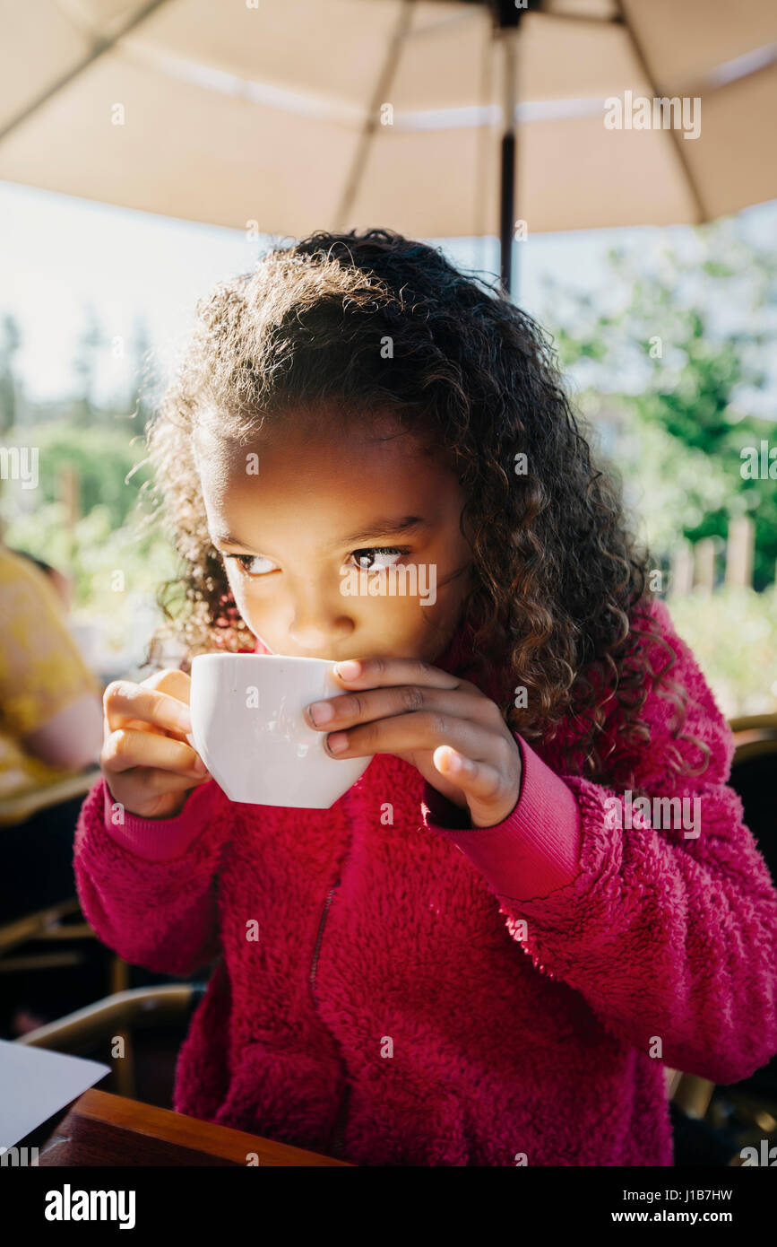 Mixed Race girl sipping from cup in restaurant Stock Photo