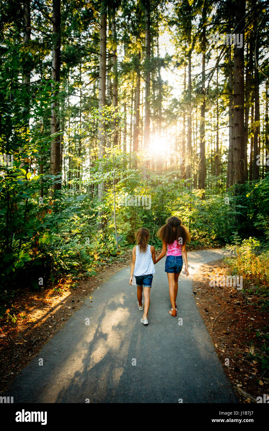 Mixed Race sisters holding hands walking on forest path Stock Photo