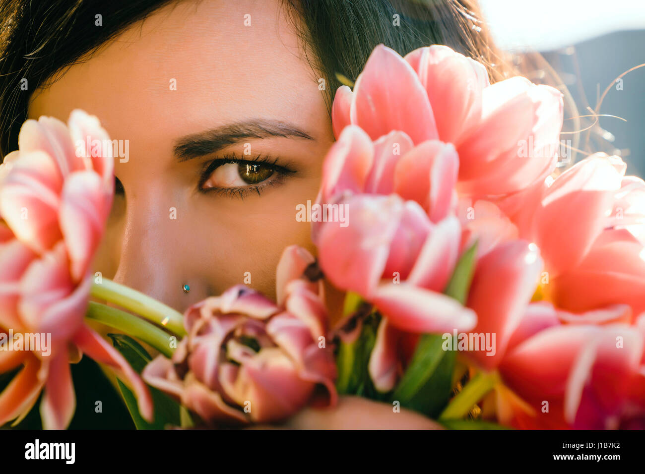 Mixed Race woman hiding face behind flowers Stock Photo