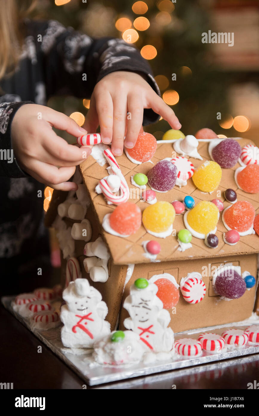 Hands of Caucasian girl decorating gingerbread house with candy Stock Photo