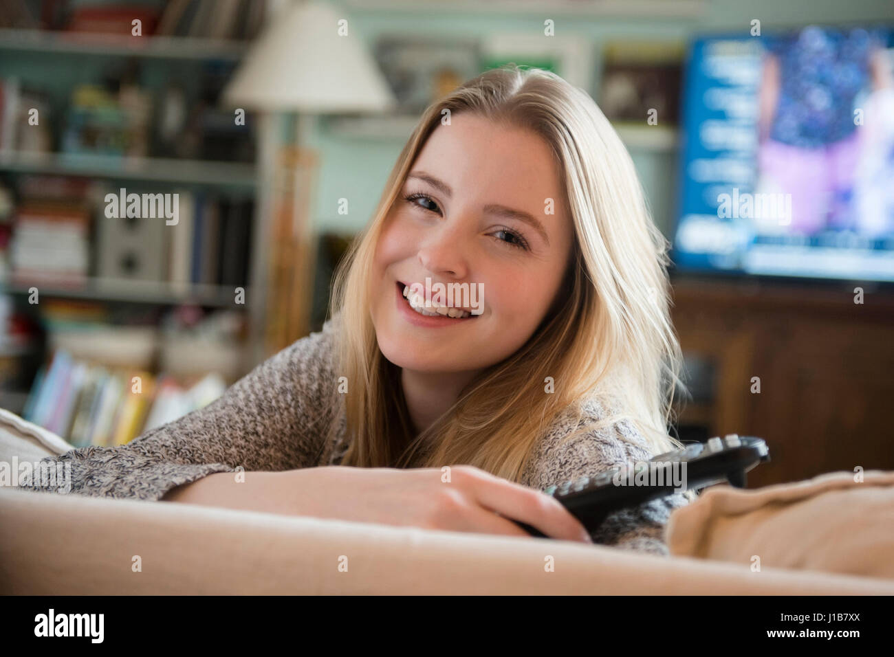 Smiling woman leaning on sofa holding remote control Stock Photo