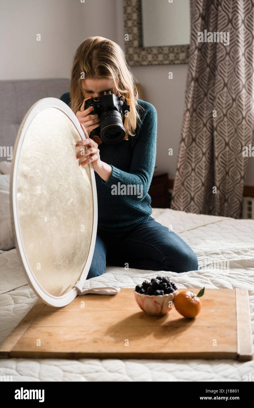 Woman kneeling on bed holding reflector photographing fruit Stock Photo