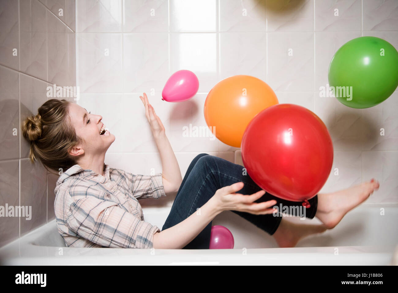Laughing woman sitting in bathtub playing with multicolor balloons Stock Photo