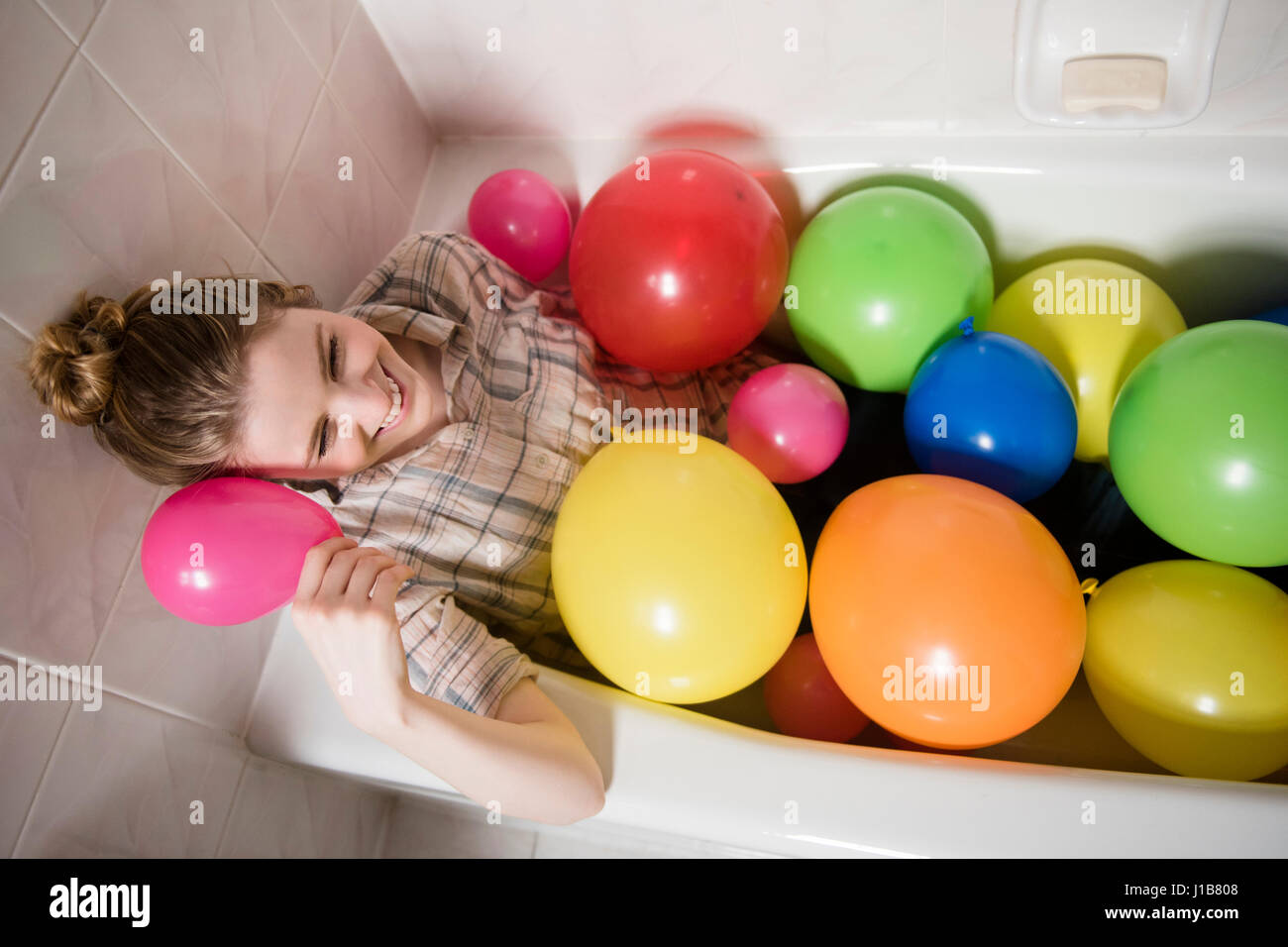 Smiling woman sitting in bathtub with multicolor balloons Stock Photo