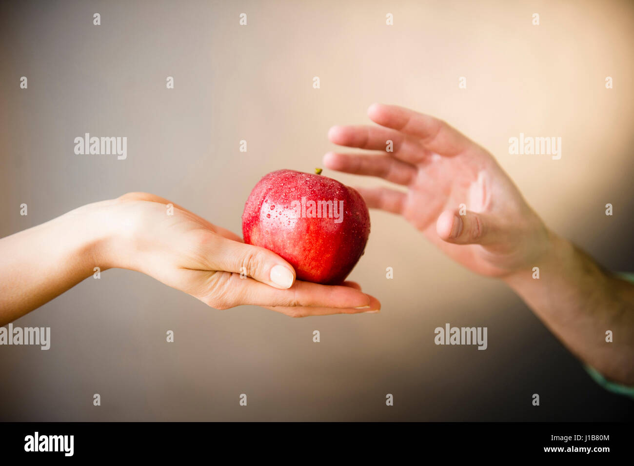 Hand of woman offering red apple to man Stock Photo