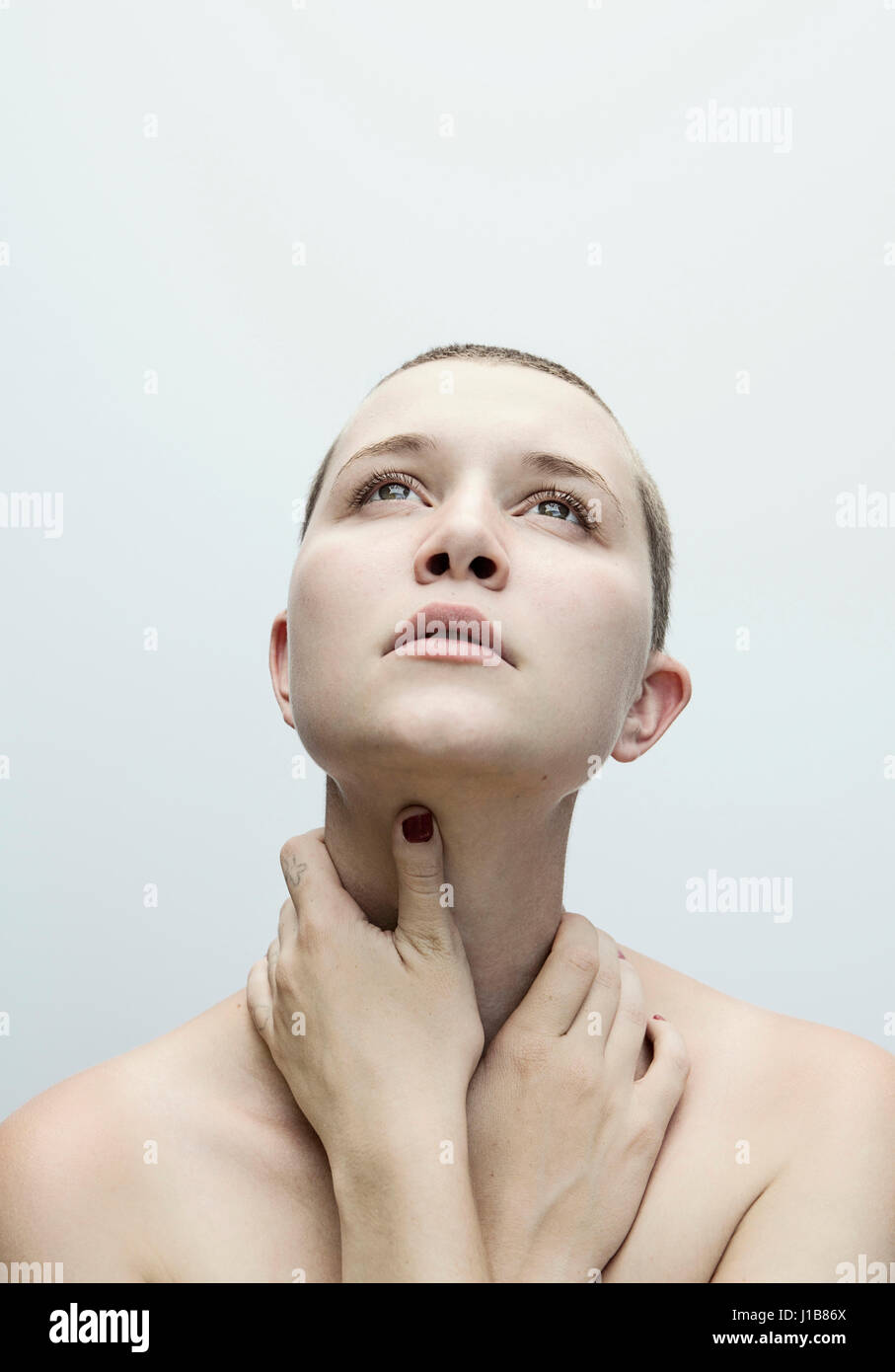 Caucasian woman with shaved-head holding neck with hands Stock Photo