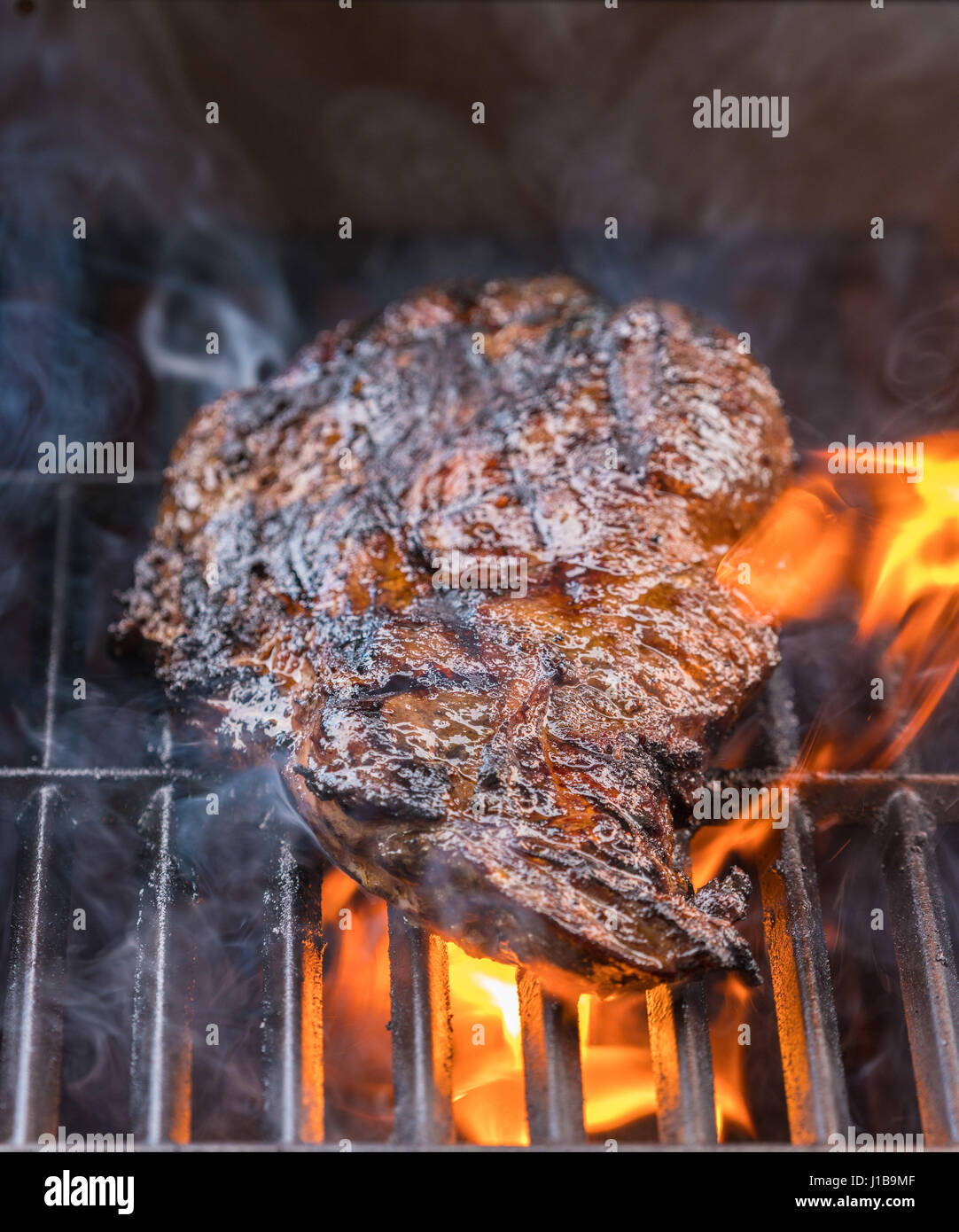 Close up of a BBQ - large piece of beef steak flaming, cooking meat outdoors on a  barbeque Stock Photo