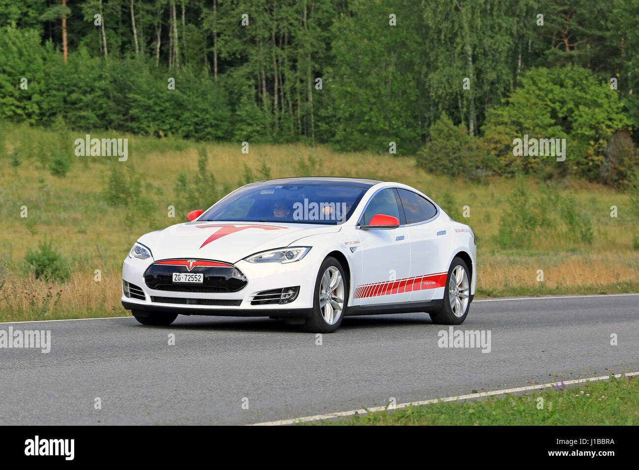 PAIMIO, FINLAND - JULY 24, 2016: Red and white Tesla Model S unique design Electric Vehicle moves along green rural road in South of Finland at summer Stock Photo