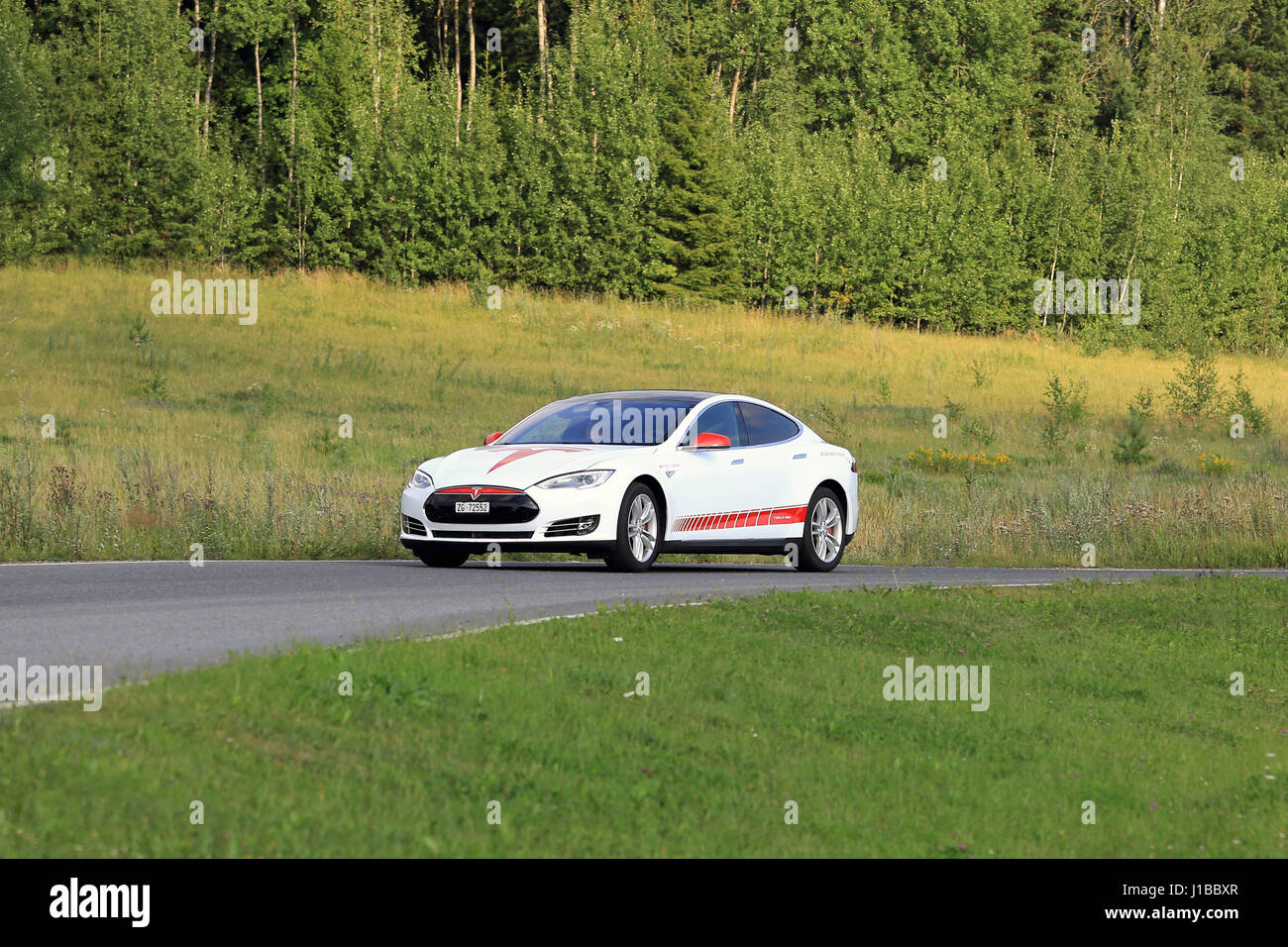 PAIMIO, FINLAND - JULY 24, 2016: Tesla Model S unique design electric car drives along rural road in South of Finland at summer surrounded by green na Stock Photo