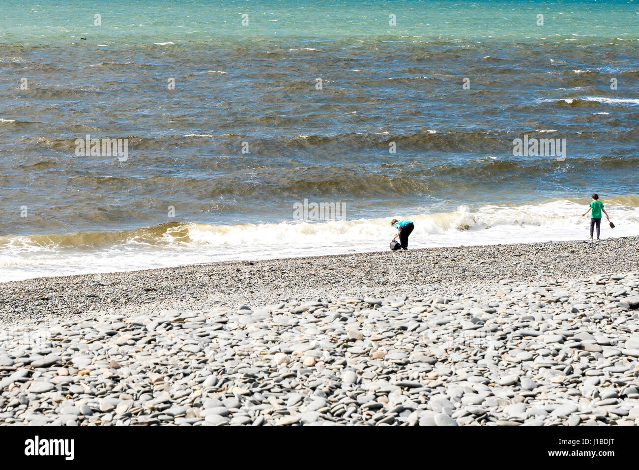 Two teenage boys playing and skimming pebbles on the beach in