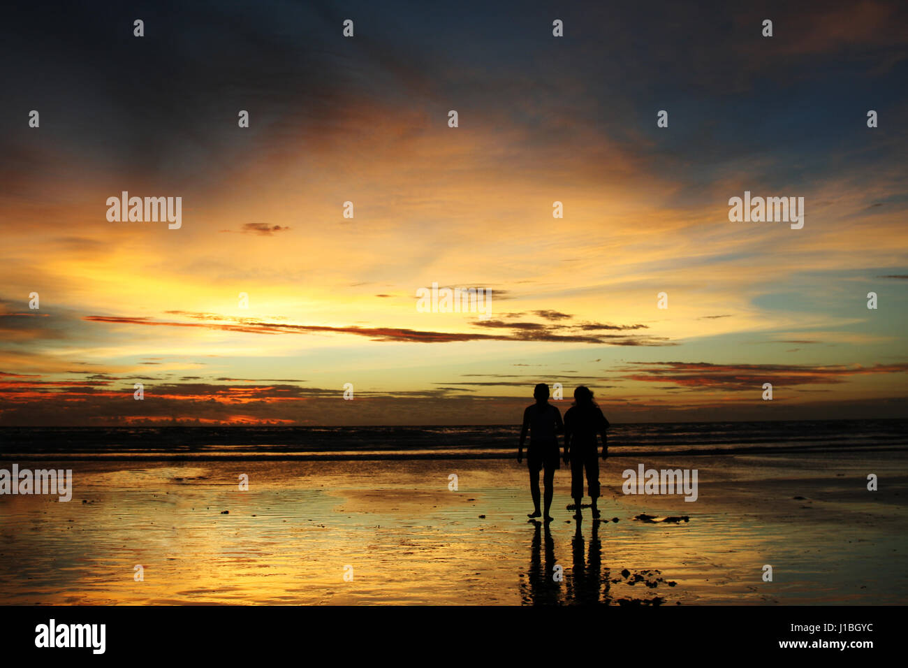 Two people in silhouette walking on a beach during sunset Stock Photo ...