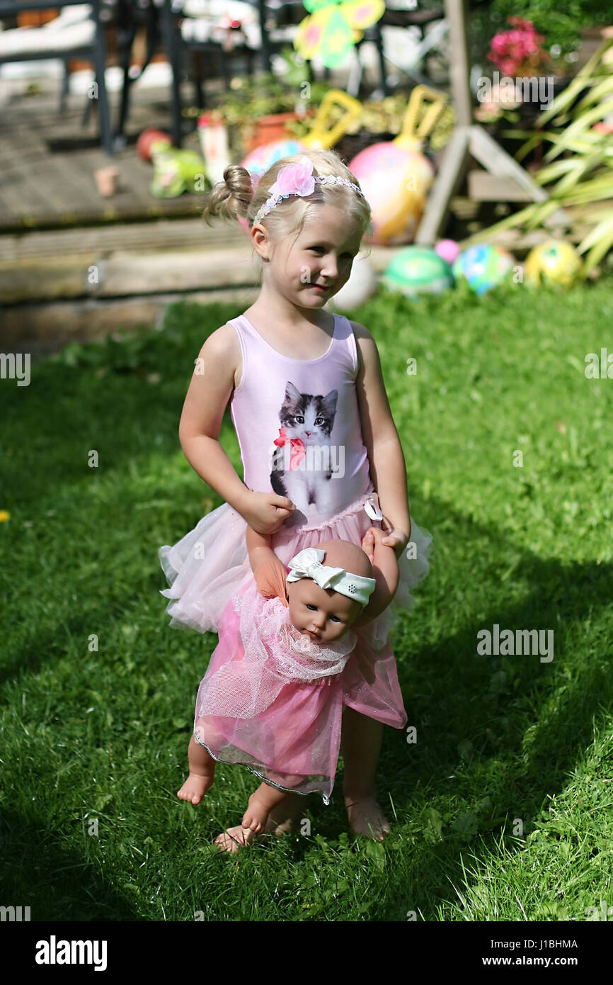 Little three year old girl, child playing with her annabel doll in the garden dressed in a tutu Stock Photo