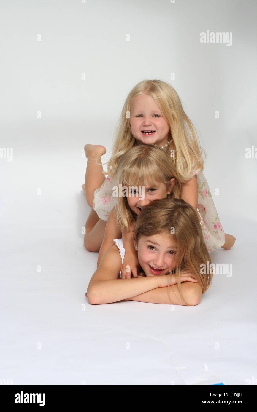 Three sisters, children kids portrait lying on their tummies, goofing and smilling and messing together, stacked up on top of each other Stock Photo