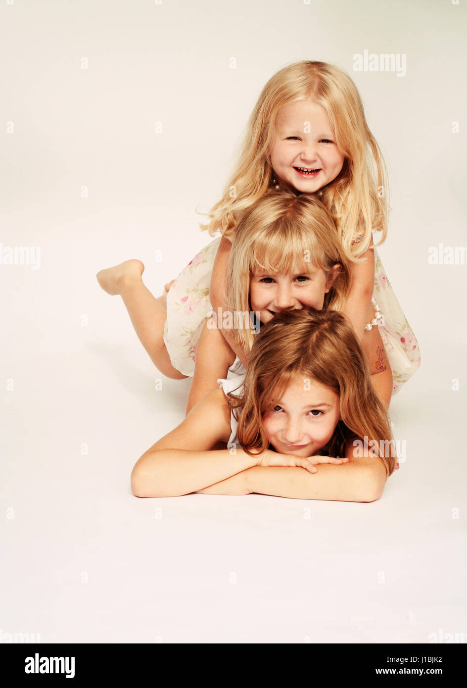 Three sisters, children portrait lying on their tummies, goofing smiling and messing together, stacked up on top of each other little blonde girls Stock Photo