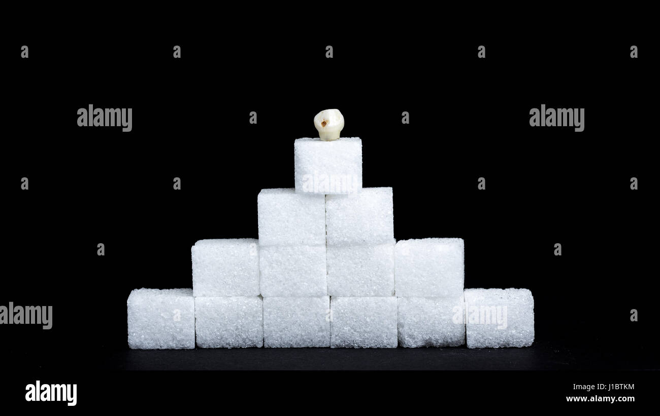 Decayed tooth on the top of a sugar cube pyramid - Concept of consuming too much sugar can cause tooth decay Stock Photo