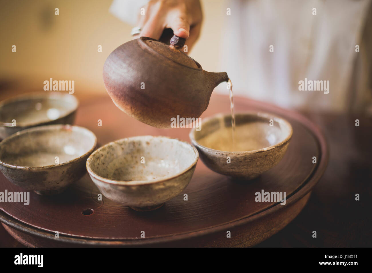 Sarah Hedden pouring tea into ceramic tea cups on a tray. Stock Photo