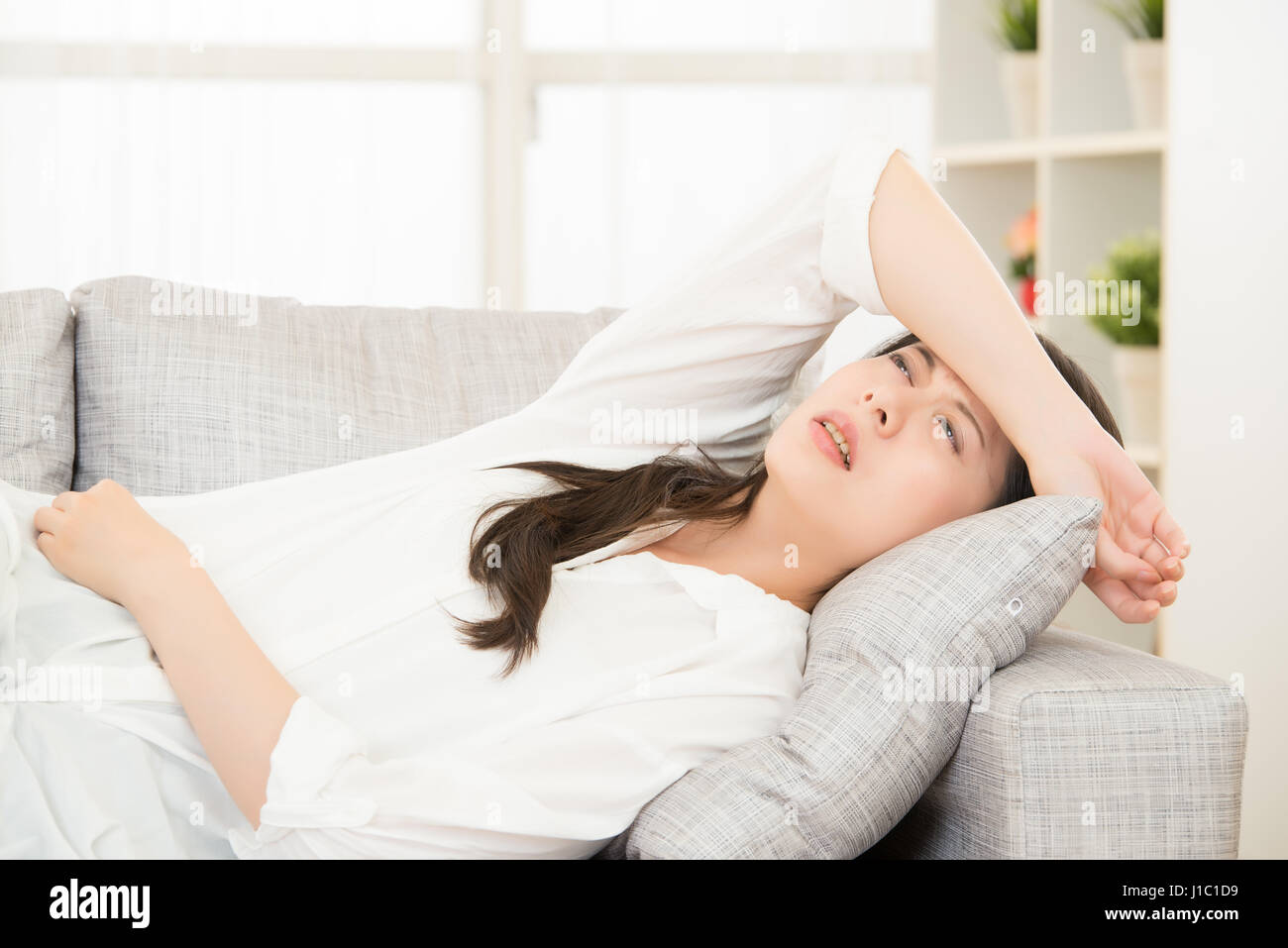 Feeling stressed. young woman touching her head while sitting on sofa at home. lifestyle and health concept mixed race asian chinese model. Stock Photo