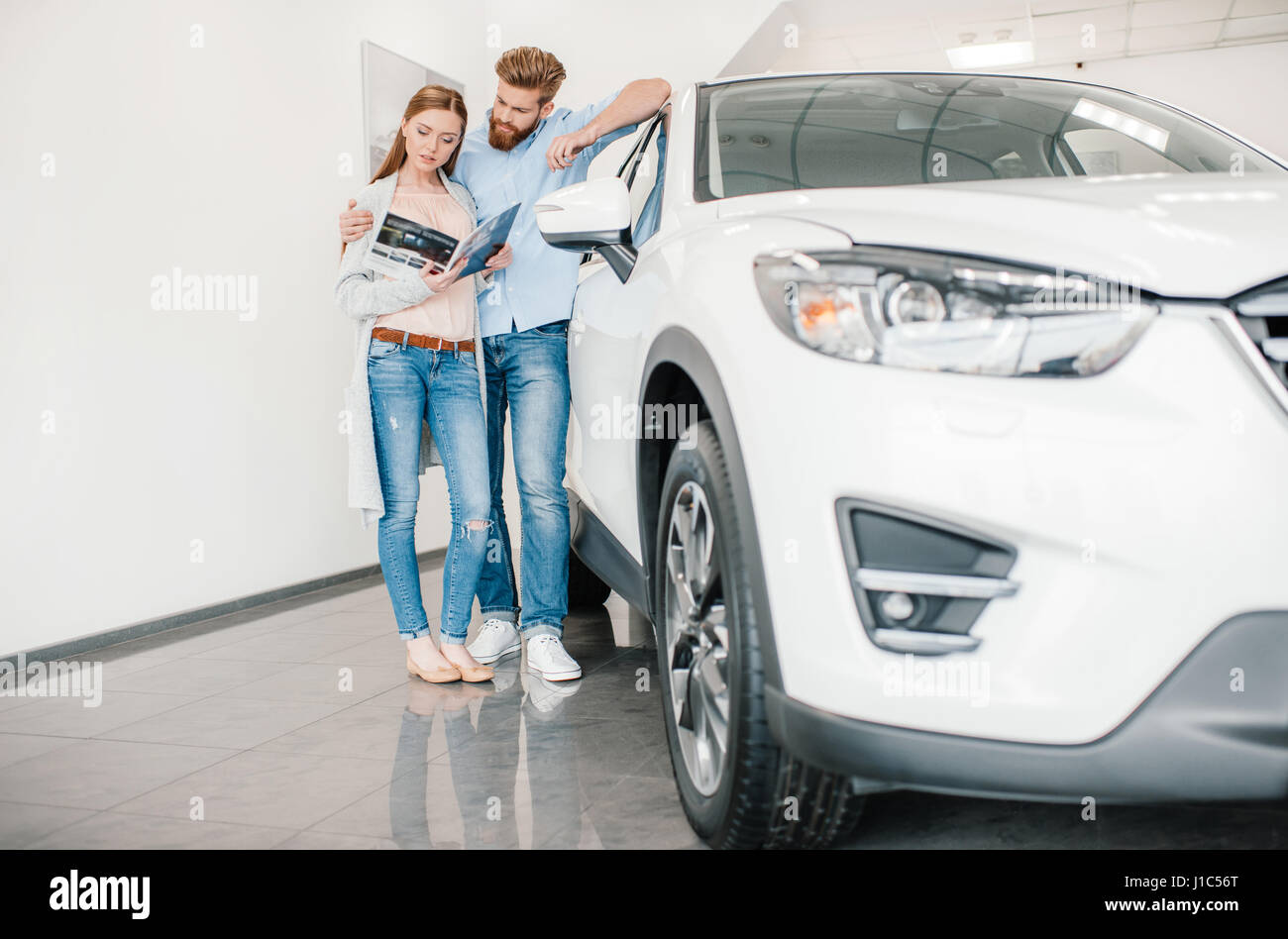pensive couple holding catalog and choosing car in dealership salon Stock Photo