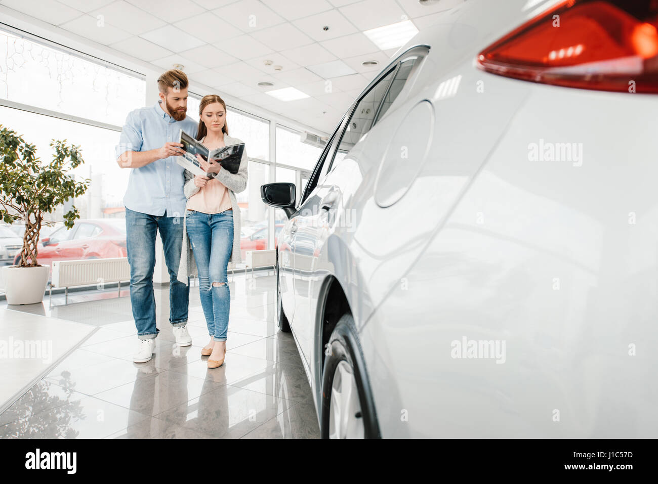 Happy couple holding catalog and choosing car in dealership salon Stock Photo